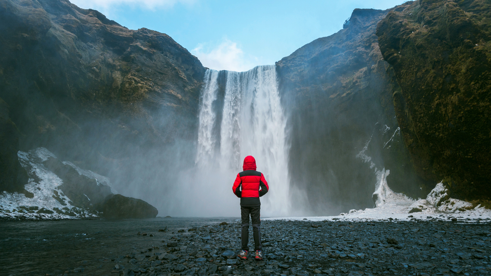 Skogafoss famous but dangerous waterfall in Iceland guy in red jacket looking towards the dangerous skogafoss waterfall